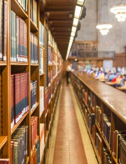 Path leads through library shelves holding many books on each side.